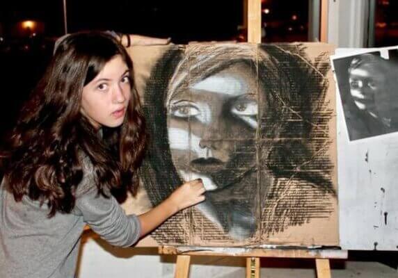 A student with dark hair holding charcoal, creating artwork on cardboard